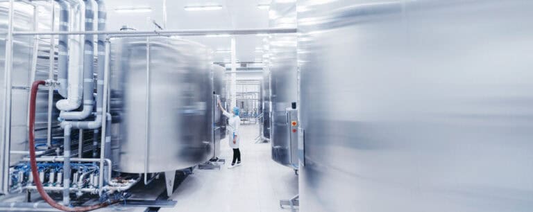 Female engineer in room of stainless steel tanks inspects control panel.