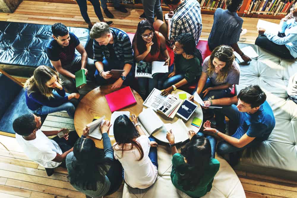 Students city around tables looking at books and chatting.