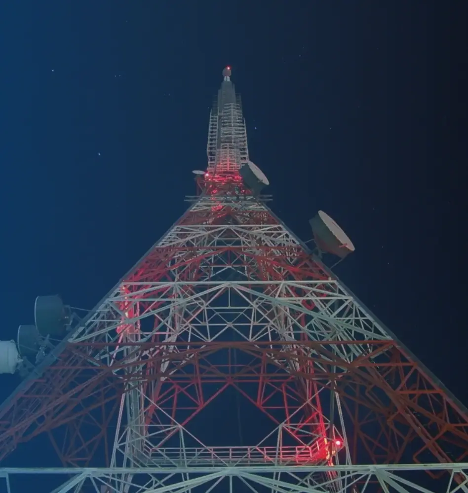Looking up at a red and white transmission tower at night.