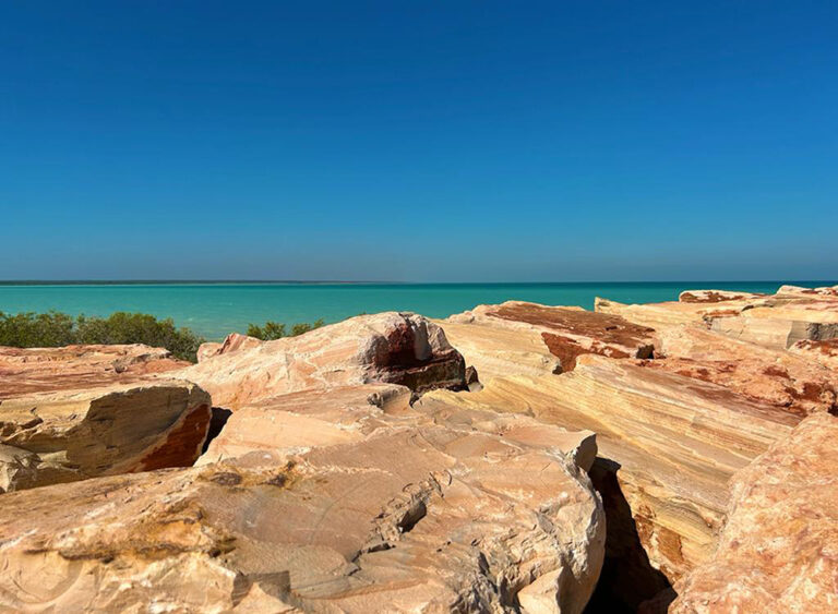 Blue ocean with red rocks in the foreground.