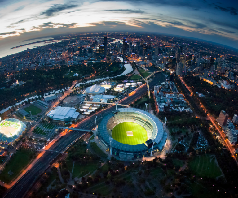 Aerial view of Melbourne at dusk with the Melbourne Cricket Ground illuminated.