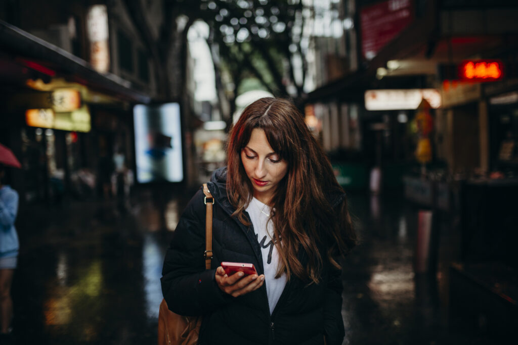 You woman looks at her smartphone against a dark, wet, city street.